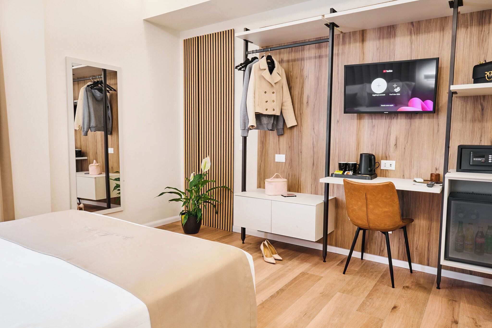 Una habitación de hotel moderna con cama, escritorio, televisor, armario y una planta.