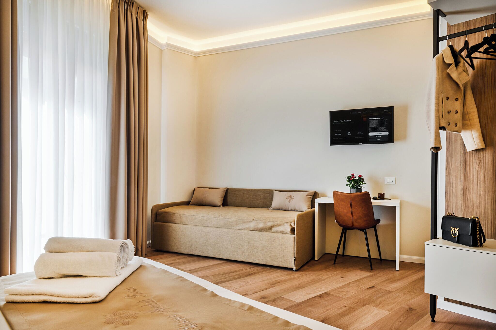 A modern hotel room with a sofa bed, a desk, a chair, and a coat rack.