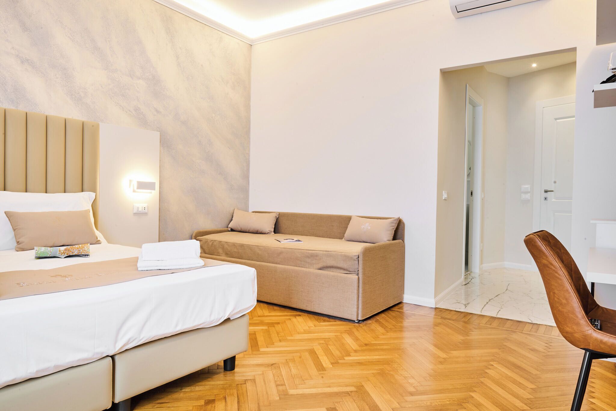 A hotel room with a bed, a sofa, a wooden floor, and a chair.