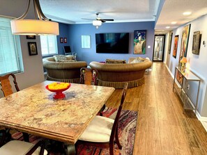 A dining area with a table, chairs, and a bowl of fruit. There are two sofas and a television in the background. - The Retreat- a perfect-sized  condo for your Bourbon Trail  adventure (Lexington)