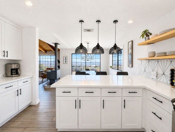 A modern kitchen with white cabinetry, a central island, pendant lighting, and a view through large windows.
