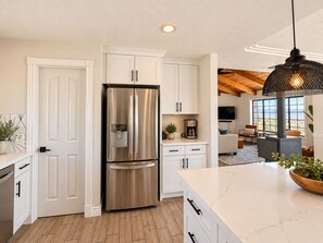 A modern kitchen with a stainless steel refrigerator, white cabinetry, and a marble countertop.