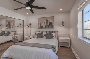 Quarto com cama grande, duas mesas de cabeceira, ventoinha no teto e obras de arte nas paredes.