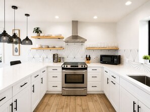 A modern kitchen with white cabinetry, a stainless steel oven, a microwave, and black pendant lights.