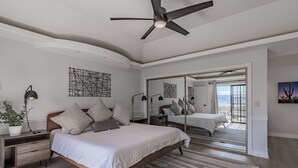 A modern bedroom with a large bed, bedside tables, a ceiling fan, and a view through a glass door.