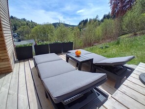 Een terras buiten met een loungeset, een tafel en plantenpotten.