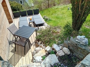 A wooden deck with a table and chairs, surrounded by a grassy yard and a stone wall. - Luxury apartment in the glass town of Lauscha with terrace, beautiful nature & mountain views (Lauscha)