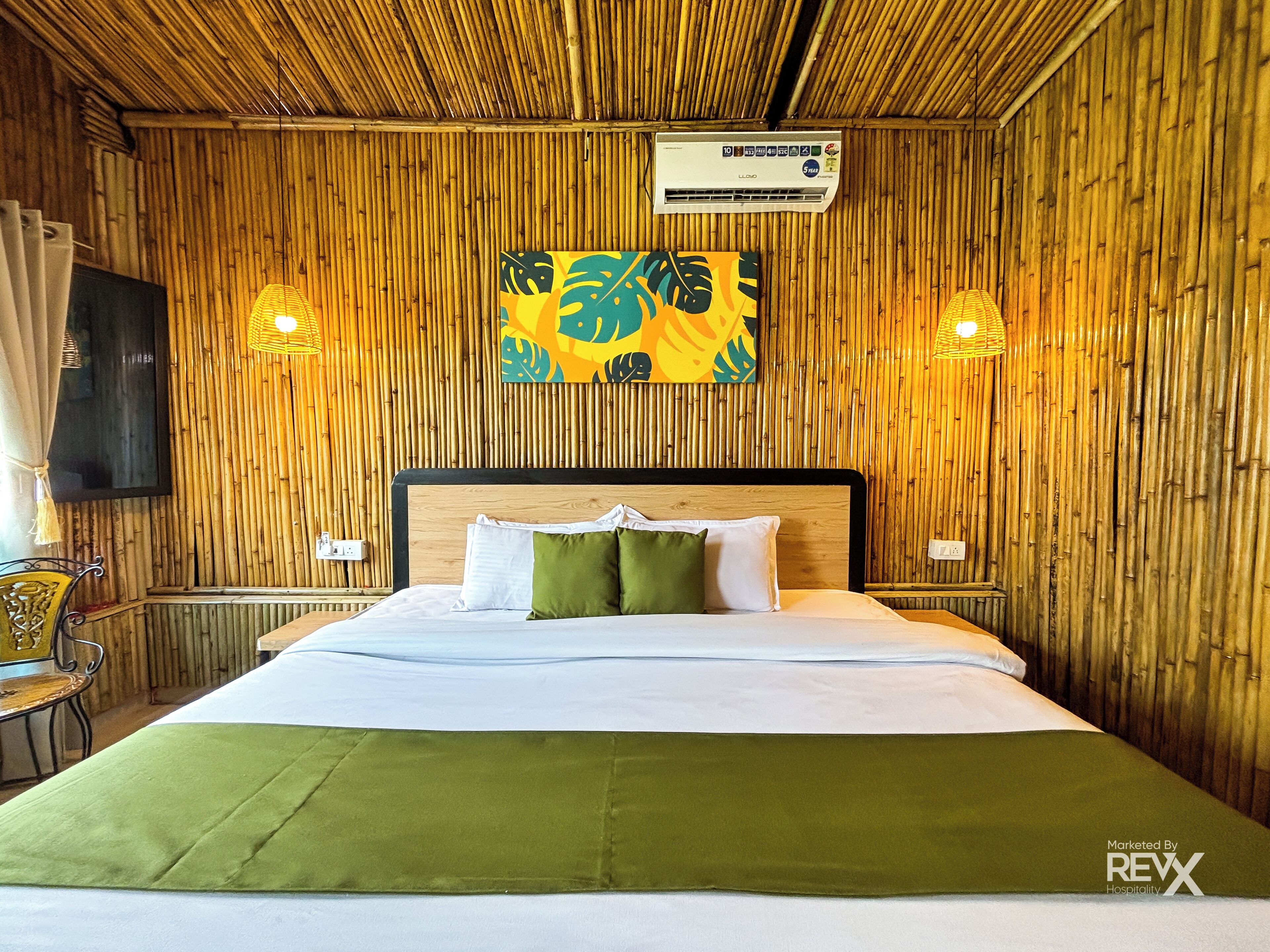 A room with a bed, a wall-mounted air conditioner, a painting, and two wall-mounted lights.