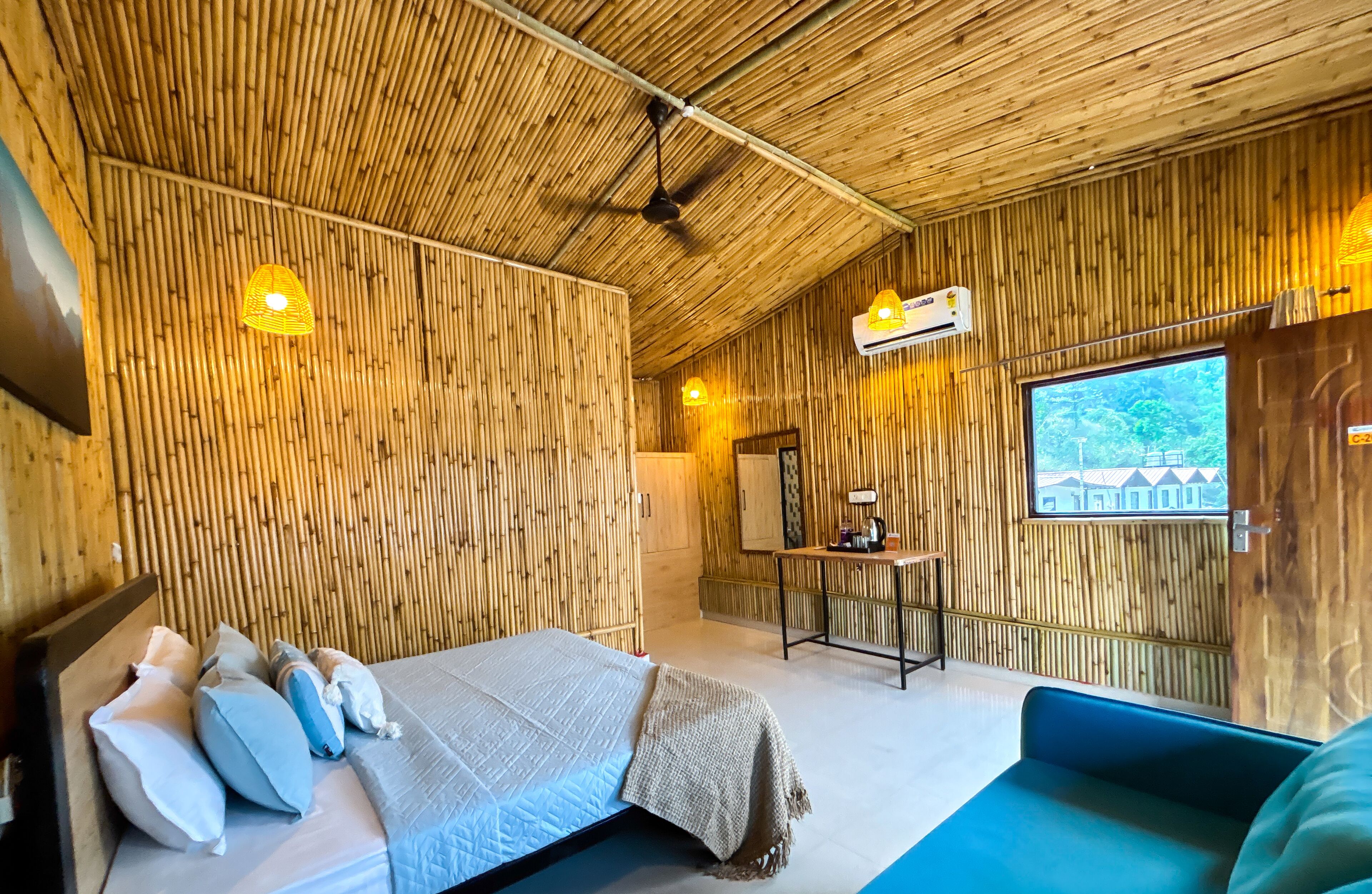 Una habitación con una cama, un sofá azul, un ventilador de techo y una ventana con vistas a edificios.