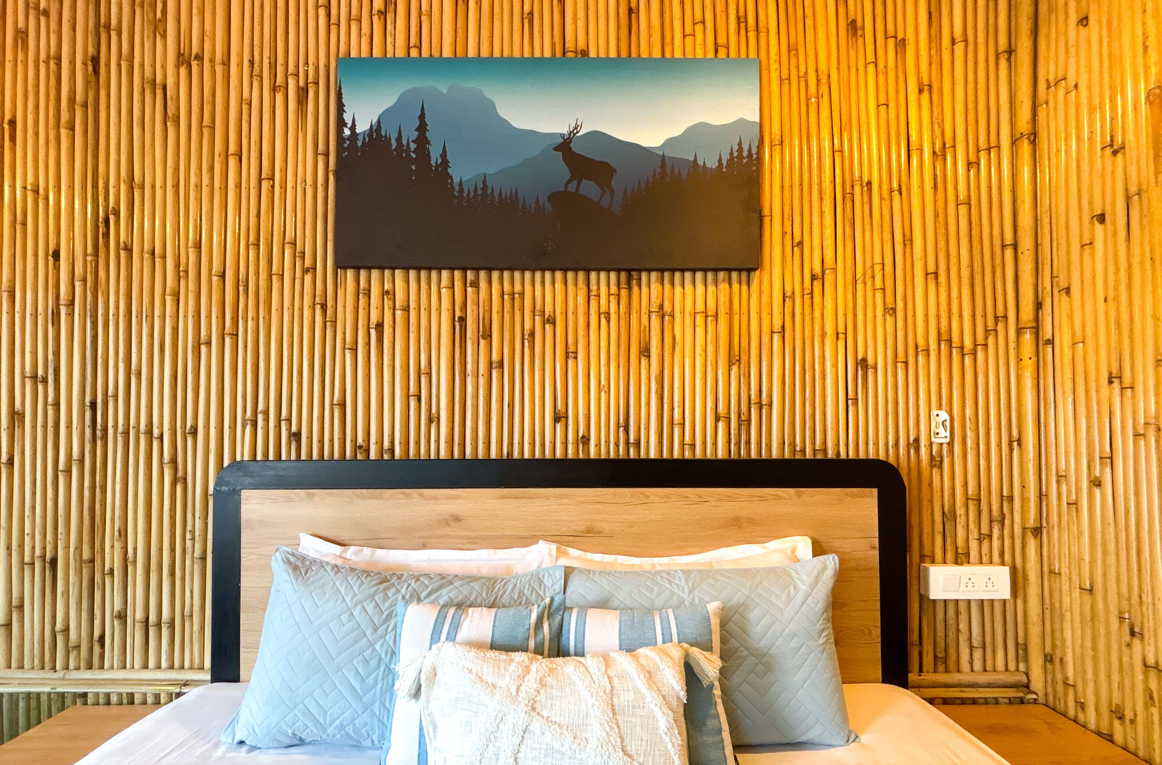 Uma cama com cabeceira de madeira, uma parede com painéis verticais de bambu e um quadro com a imagem de um veado numa montanha.