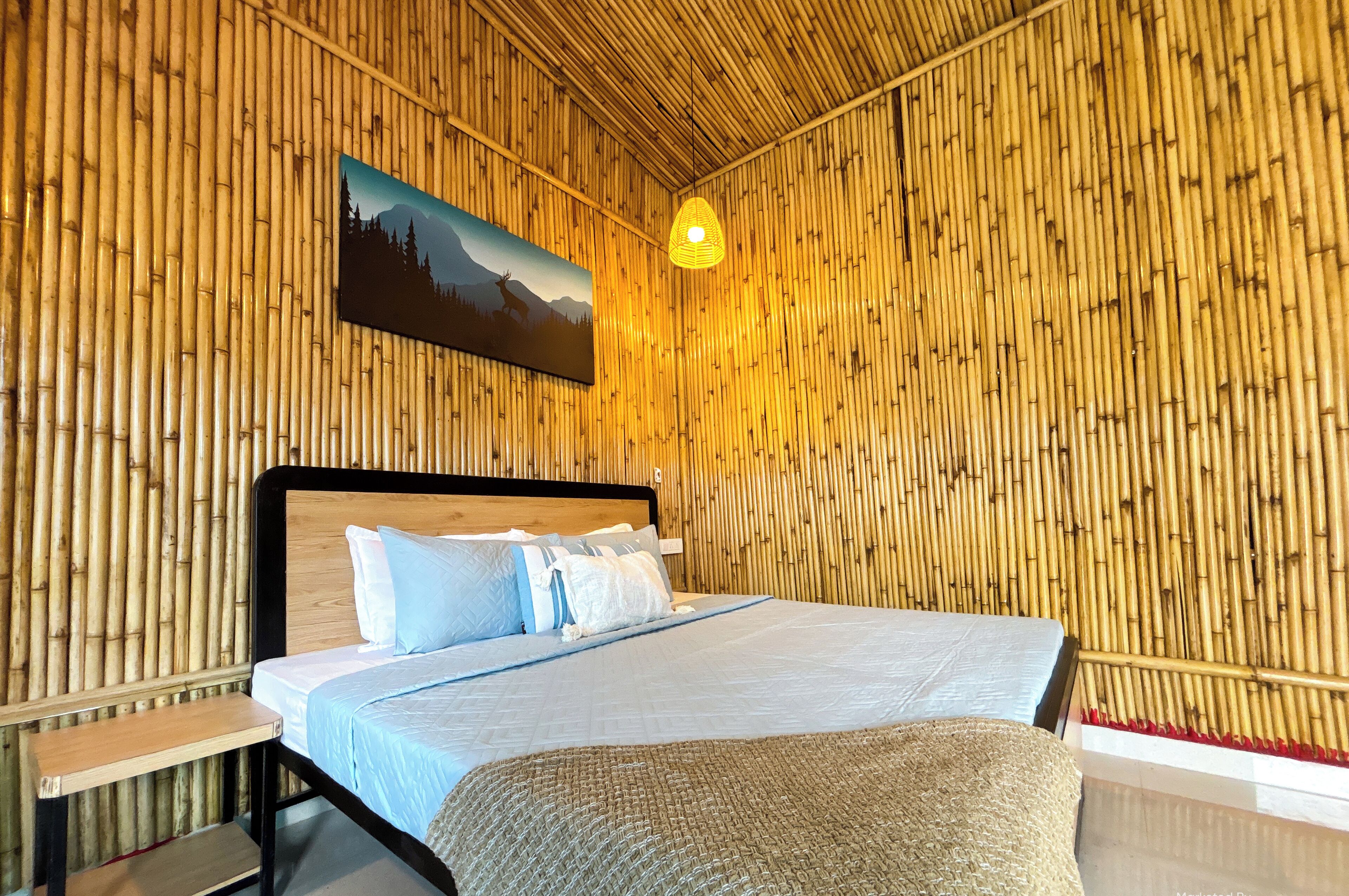 A room with a bed, a nightstand, a bench, a hanging light fixture, and a wall-mounted painting.