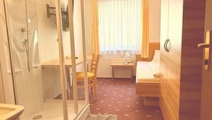 A compact hotel room with a glass-enclosed shower, a bed, a bedside table, and a wardrobe. - Pension Plattenhof - 11 (Telfs)