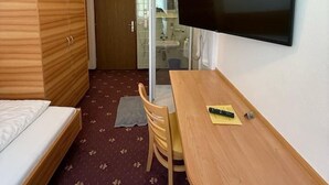 A compact hotel room with a bed, a desk, a chair, a television, and a bathroom visible through an open door. - Pension Plattenhof - 11 (Telfs)