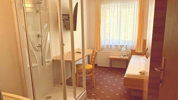 A compact hotel room with a shower enclosure, a small table, a chair, and a bed. - Pension Plattenhof - 11 (Telfs)