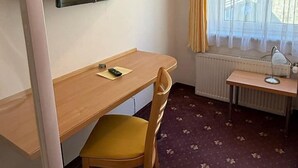 A hotel room with a wooden desk, a chair, a television mounted on the wall, a small table with a lamp, and a window with curtains. - Pension Plattenhof - 11 (Telfs)