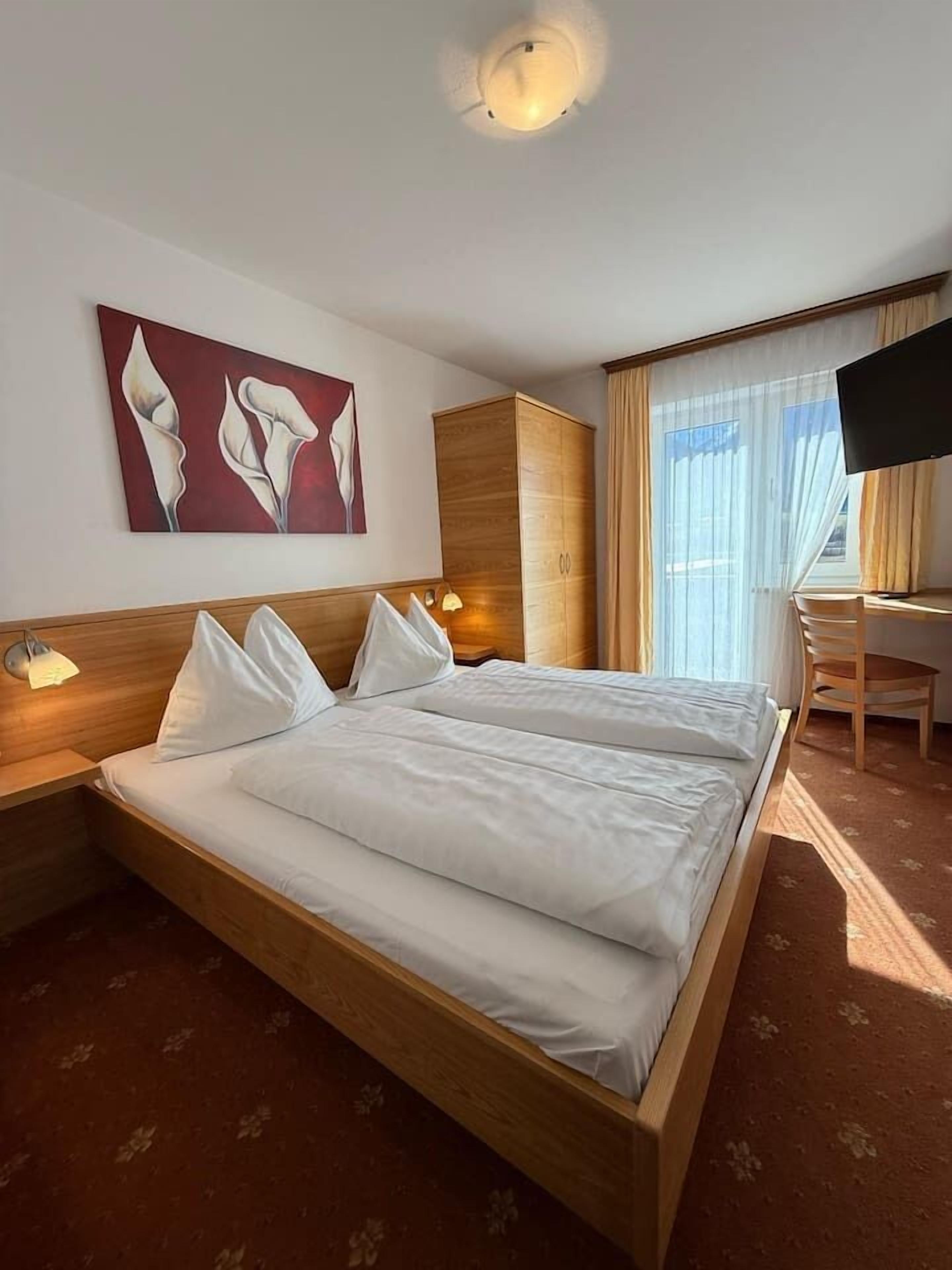 Een hotelkamer met een groot bed, een bureau, een televisie en een schilderij aan de muur.