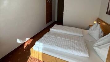 A hotel room with a double bed, a wooden wardrobe, and a small desk with a lamp.