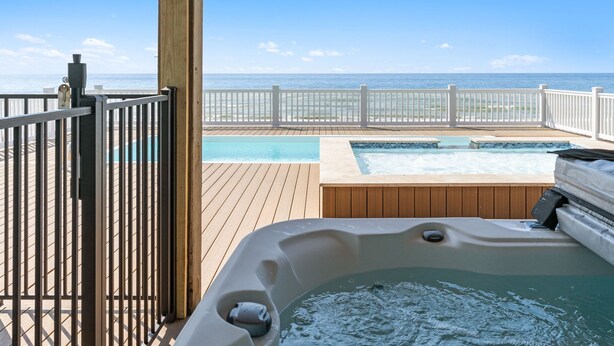 A wooden deck with a hot tub, a pool, and a view of the ocean. - Arches: Oceanfront retreat in Oak Island, 4BR, 3BA, sleeps 12, ideal for families. (Oak Island)