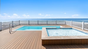 A wooden deck with a pool and hot tub, white railings, and a view of the ocean. - Arches: Oceanfront retreat in Oak Island, 4BR, 3BA, sleeps 12, ideal for families. (Oak Island)