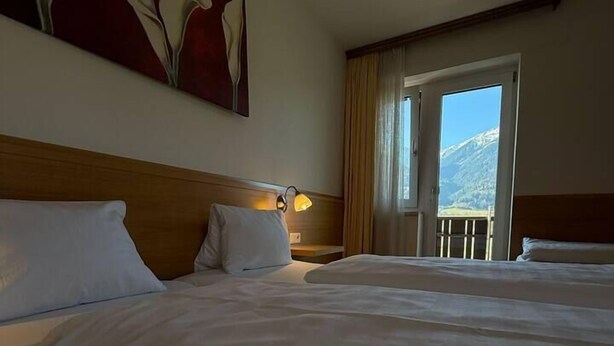 A hotel room with two beds, a painting on the wall, a lamp, and a view of mountains through the window.