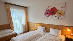 Habitaci ón de hotel con dos camas, un ventanal con cortinas, un cuadro de flores en la pared y lámparas de noche.