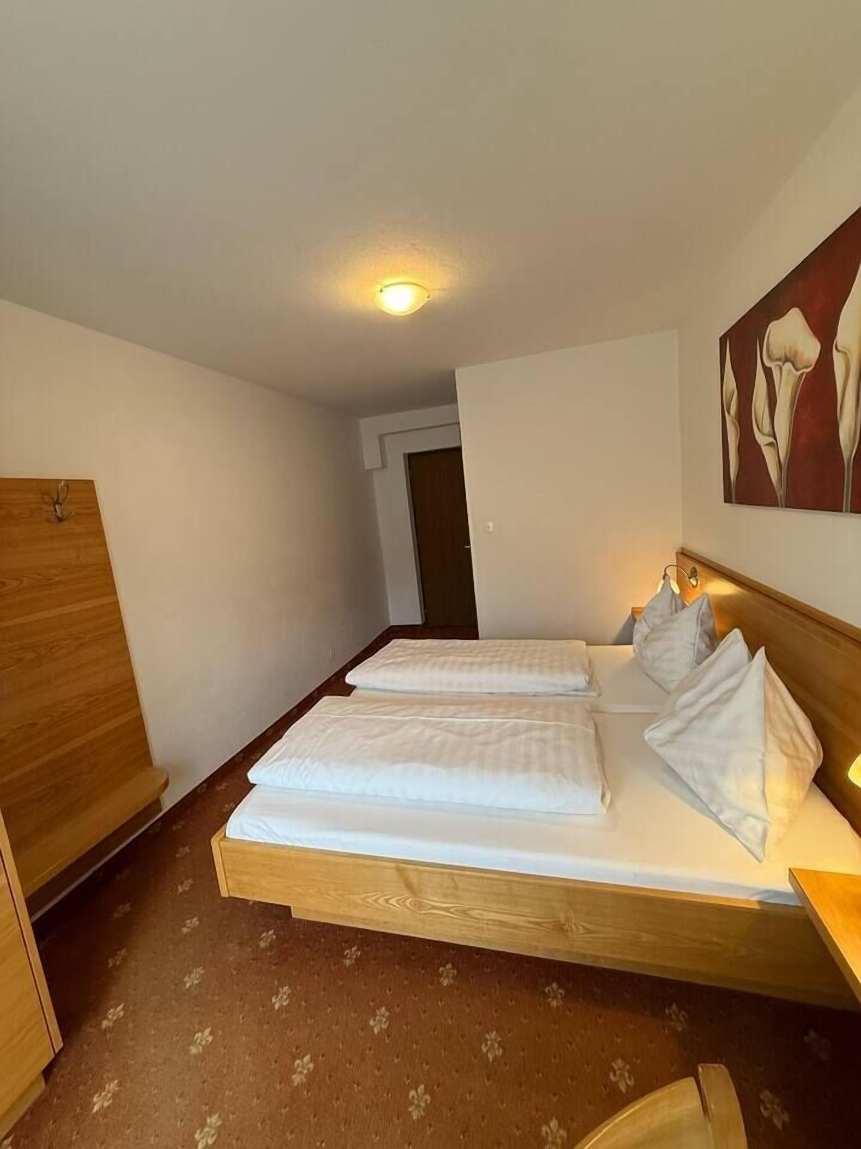 Une chambre d’hôtel avec deux lits simples, une armoire en bois, une moquette à motifs floraux et un tableau au mur.