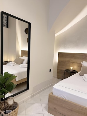 A modern bedroom with a large mirror, a bed with white linens, a bedside table with a lamp, and a plant.