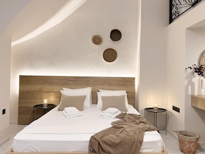 A modern bedroom with a wooden headboard, two bedside tables with lamps, a bed with neatly folded white towels, and a woven basket on the floor.