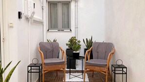 Un petit espace extérieur aménagé avec des sièges, comprenant deux fauteuils en osier, une petite table et des plantes en pot.