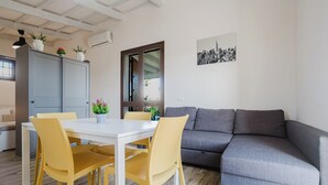 Ein modernes Wohnzimmer mit einem grauen Sofa, einem weißen Esstisch mit gelben Stühlen und einem grauen Schrank mit Pflanzen.