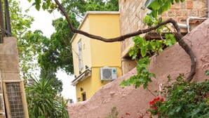 A courtyard with potted plants and flowers, stone flooring, and a building with a yellow facade. - Arionos Rooms (Rhodes)