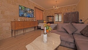 A living room with a stone wall, a large flat-screen TV, a wooden cabinet, a marble coffee table, a purple sofa, and a chandelier. - Arionos Rooms (Rhodes)