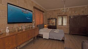 Ein Zimmer mit einem Bett, einem an einer Steinwand montierten Fernseher, einem Holzschrank und einer Kandelaberleuchte.