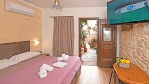 A hotel room with a bed, a television, a table with fruits, and a view of the outside. - Arionos Rooms (Rhodes)