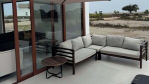 A modern outdoor seating area with a sofa and a table, a large umbrella, and a view of the beach. - Beachfront Elegance: Private Pool & Steps to Shore (Chincha Baja)