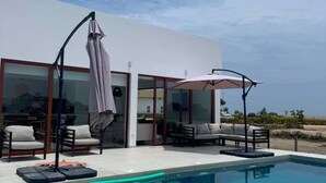 A modern outdoor pool area with a glass-enclosed patio, lounge chairs, and umbrellas. - Beachfront Elegance: Private Pool & Steps to Shore (Chincha Baja)