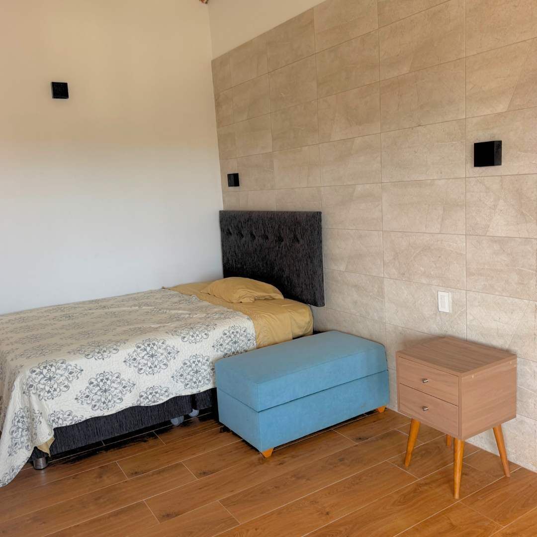 Una camera da letto con un letto, una panca blu, un comodino in legno e un muro rivestito di piastrelle.