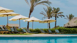 A pool area with lounge chairs and umbrellas, surrounded by palm trees.