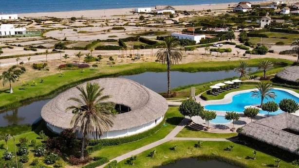 A resort with a circular pool, palm trees, and a beach in the background.