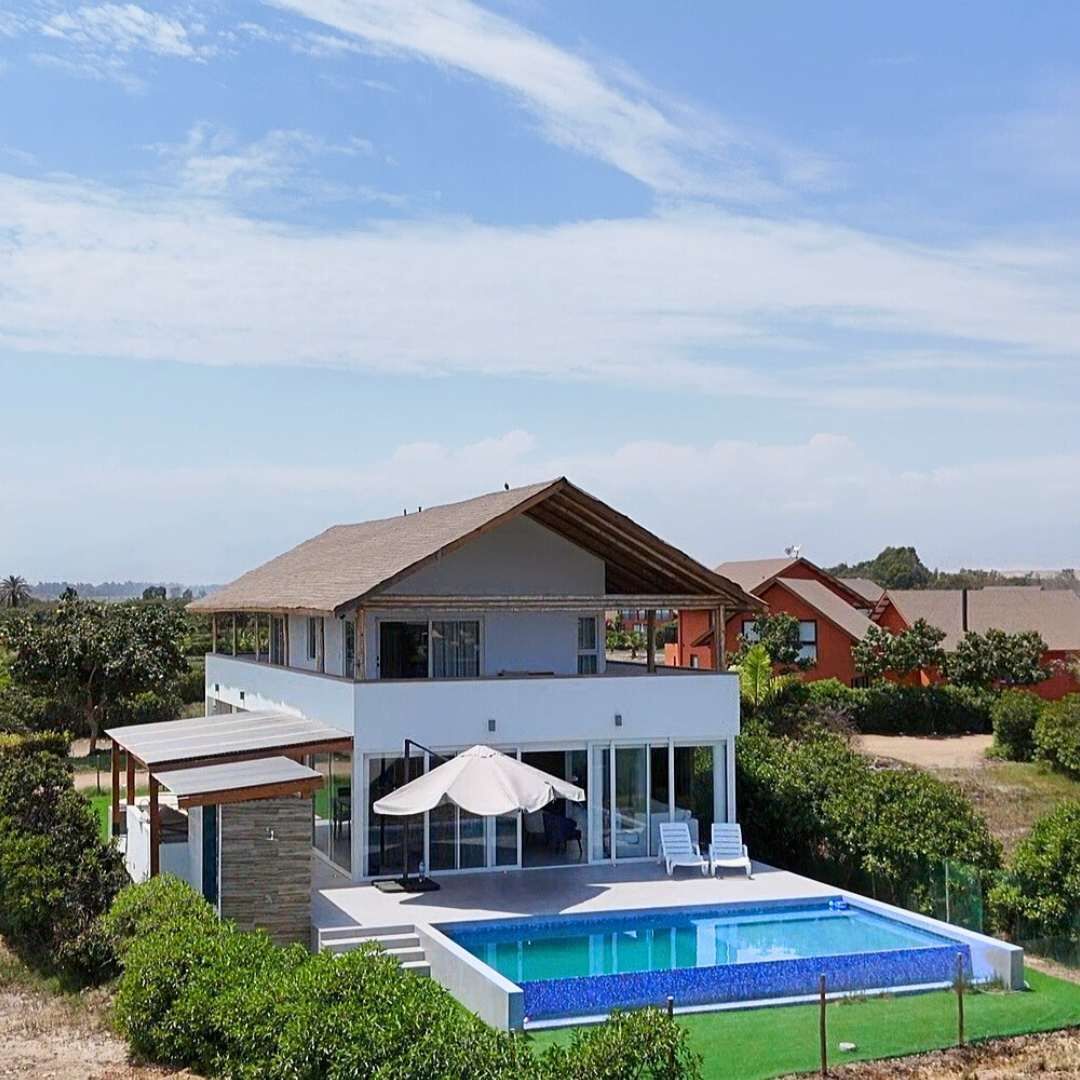 Ein modernes, zweistöckiges Haus mit Schwimmbad, umgeben von Grünflächen und weiteren Häusern im Hintergrund.