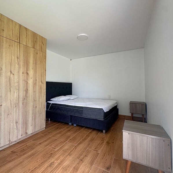 Un dormitorio con cama, armario de madera y una pequeña alacena.