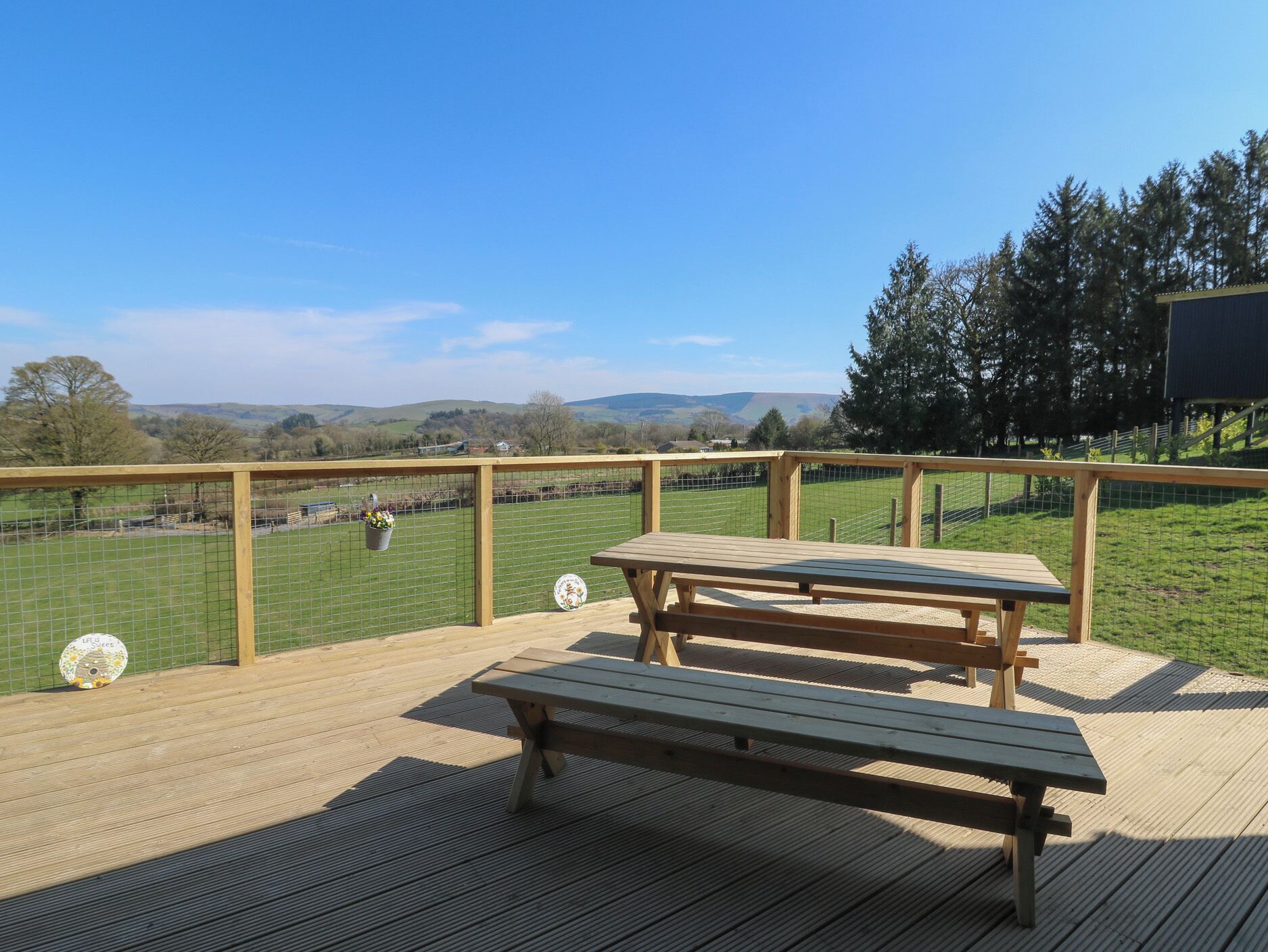 A wooden deck with a picnic table and a view of a fenced field.