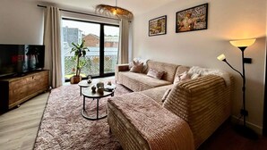 A living room with a sofa, a coffee table, a TV, and a plant. - Apartment in Spa Near Thermes & Circuit (Spa)