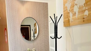 A hallway with a wooden floor, a black coat stand, a round mirror, and a black console table with a plant. - Apartment in Spa Near Thermes & Circuit (Spa)