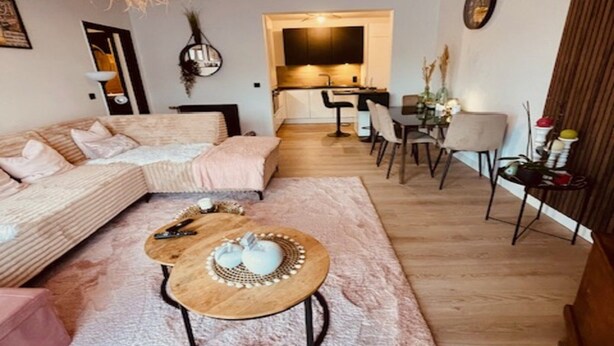 A modern living room with a sofa, a coffee table, and a dining area with chairs. - Apartment in Spa Near Thermes & Circuit (Spa)