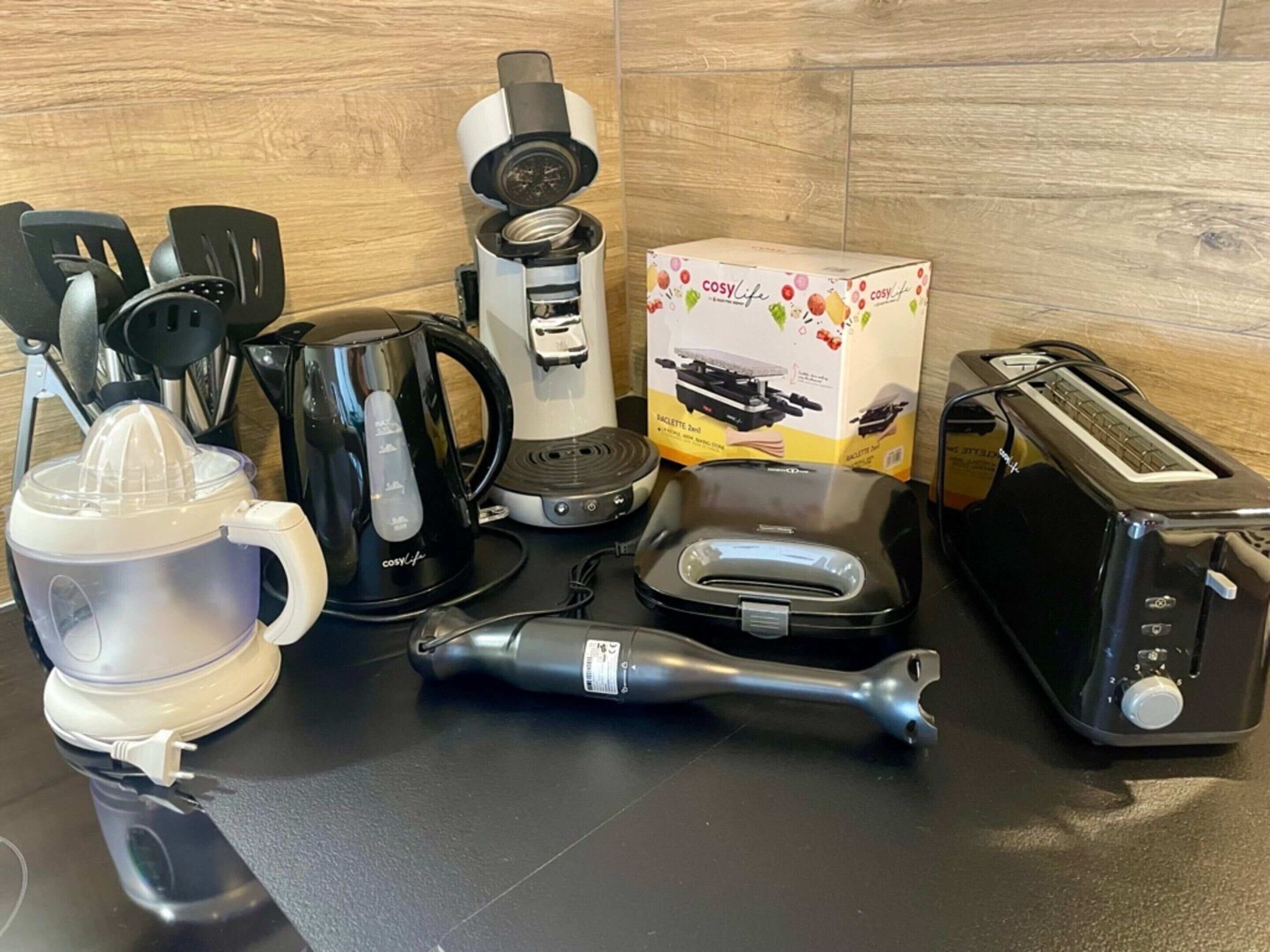 A kitchen counter with a coffee maker, toaster, kettle, and a box of a kitchen appliance.
