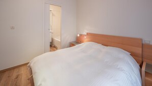 A bedroom with a wooden headboard, a white bedspread, and a wooden floor.
