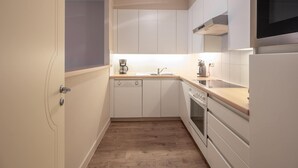 A compact kitchen with white cabinets, a built-in oven, a microwave, and a coffee maker.