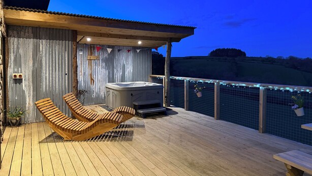 Une terrasse en bois avec deux chaises longues, un jacuzzi et une vue sur la campagne.