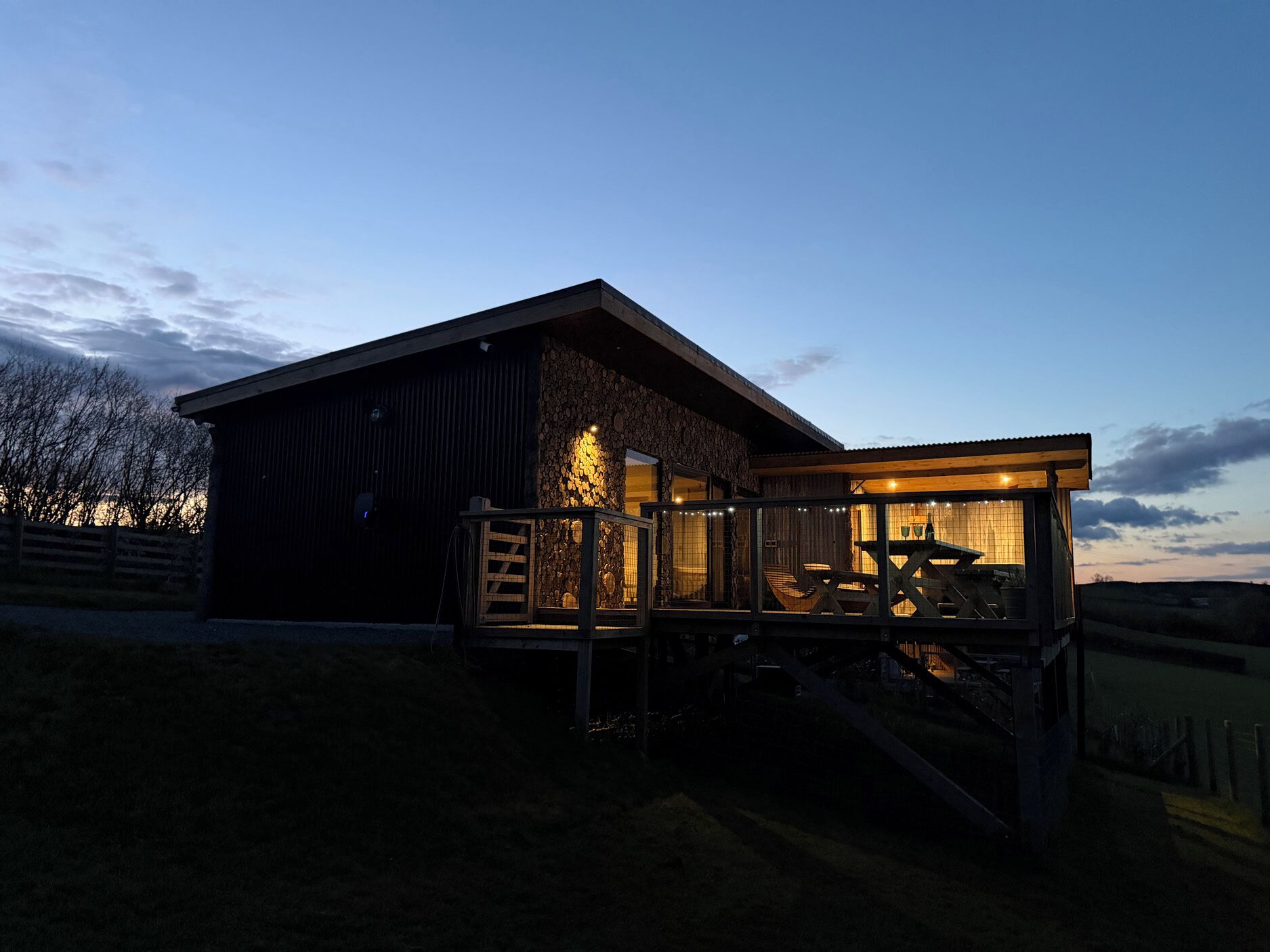A rustic cabin with a wooden deck, a stone wall, and a large window.